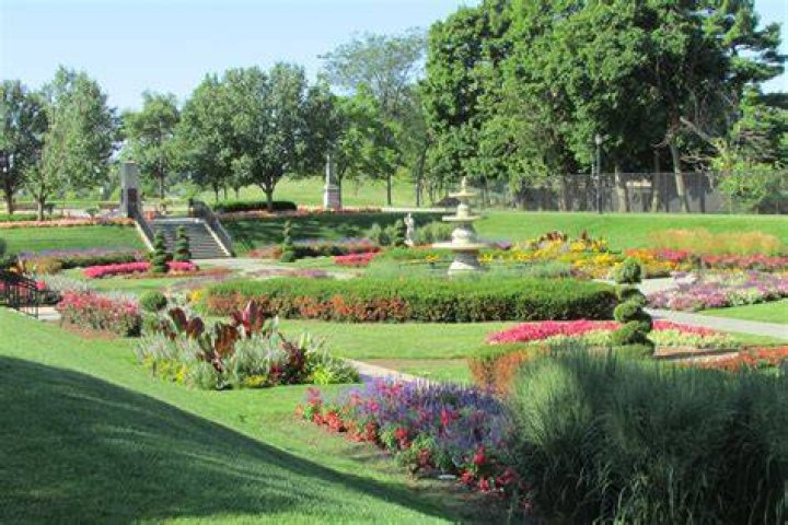 An image of a park island layout in Animal Crossing new horizons featuring fruit trees, flowers, a lake and a fountain