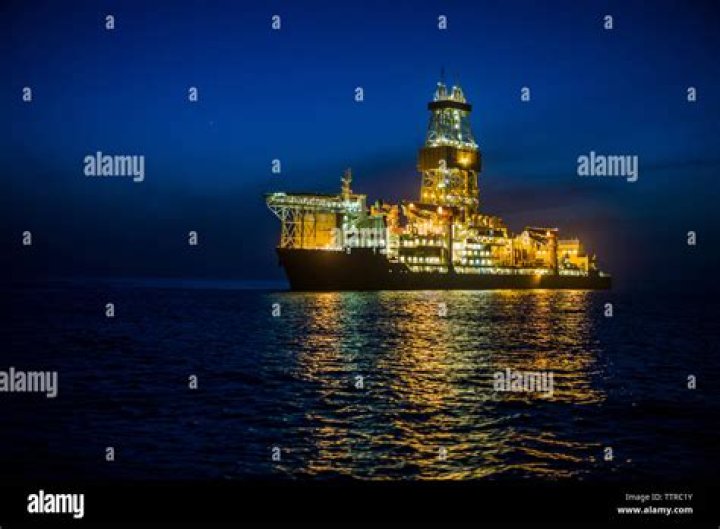 Illuminated drill ship on sea against sky at night stock photo